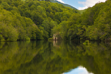 En medio del embalse de Santa Fe, en Montseny, Cataluña, se alza una antigua edificación parcialmente oculta entre la densa vegetación verde que rodea el lago