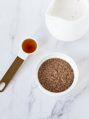 Ground flaxseed (linseed), maple syrup and vegan milk on white marble background. Top view. Plant-based ingredients for healthy breakfast preparation.