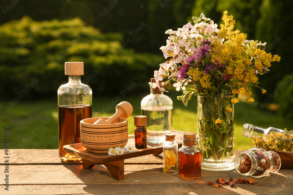 Wall mural different tinctures in bottles, ingredients, mortar and pestle on wooden table outdoors