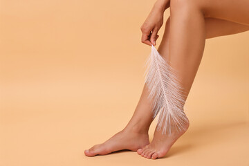 Woman with smooth legs and feather on beige background, closeup. Space for text