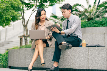 Obraz premium A male and female business team engage in discussion utilizing a laptop and notes. team sitting at outdoor pedestrian landscape. reflecting the importance of collaboration and strategic planning.