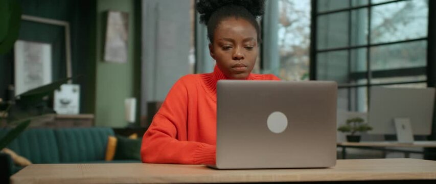 360 degree time-lapse office. Footage of good-looking brunette African American girl in casual clothes using laptop. Focused young woman typing on keyboard of laptop at work. Camera moving around