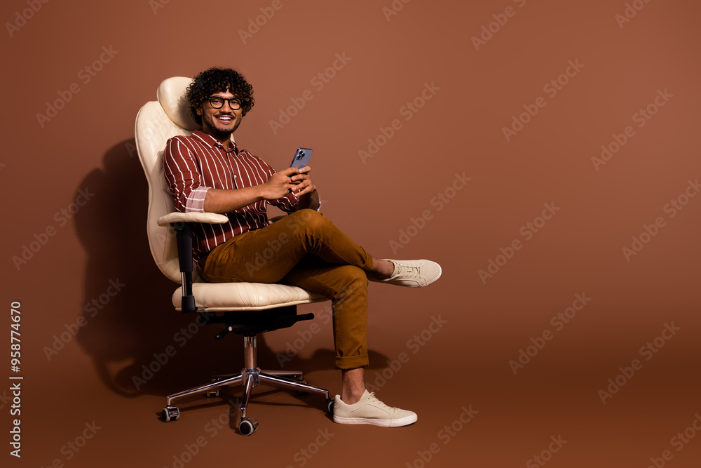 Poster full body portrait of nice young man sit chair use phone empty space wear striped shirt isolated on 