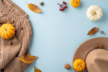 Flat lay of autumn elements including pumpkins, a sweater, and a hat on a blue background. Perfect for seasonal and cozy fall themes