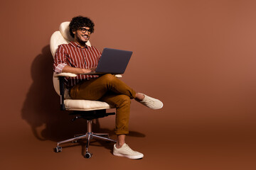 Full body portrait of nice young man sit chair laptop wear striped shirt isolated on brown color background