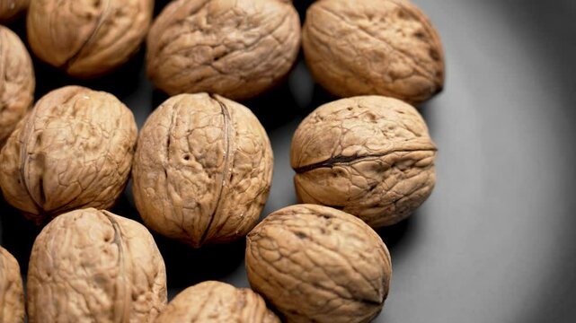 Freshly harvested walnuts gathered from the orchard on a black ceramic plate close up. Rotation