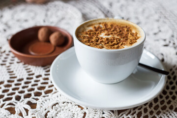 A cup of spiced cocoa on a lace tablecloth alongside sweet treats in a cozy setting