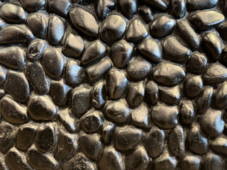 Close up of black rubbles stones or round cobble stones cemented and stacked on a wall, in black glossy paint finish.