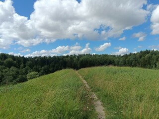 Bubiai hill during sunny day. Small hill. Grass is growing on hill. Staircase leading to the top. Sunny day with white and gray clouds in sky. Nature. Bubiu piliakalnis.