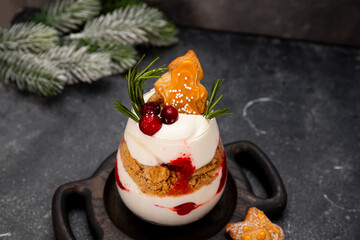 A glass of Christmas dessert with gingerbread cookies, whipped cream and cranberries on grey background
