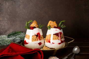 Two glasses of Christmas dessert with gingerbread cookies, whipped cream and cranberries on dark background