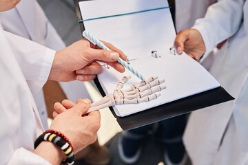 Close up on hands of med student examining anatomical model of human hand skeleton pointing with...