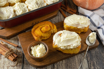 Freshly baked pumpkin cinnamon rolls or cinnabon with cream cheese on a rustic wooden table. Homemade seasonal autumn homemade pastry.