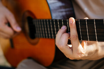 young man is playing acoustic guitar outside on summer