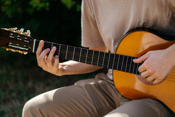 young man is playing acoustic guitar outside on summer