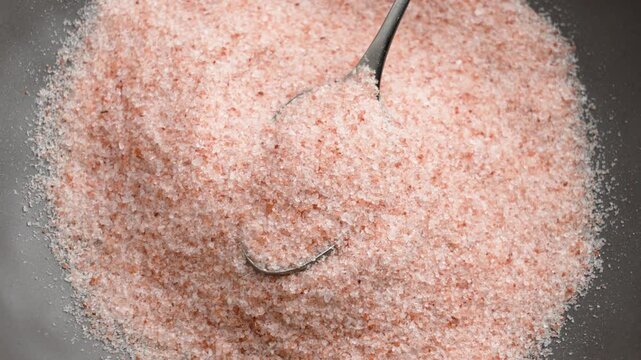 Crushed Himalayan pink mineral salt in a metal spoon. Fresh raw exotic culinary ingredient. Top view. Rotation