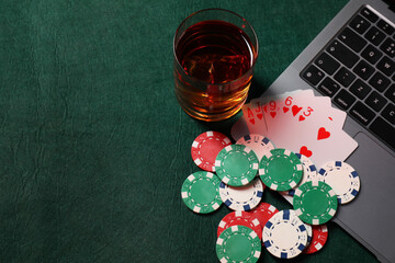 Poker chips, laptop, playing cards and glass of alcohol drink on green table, flat lay. Online game
