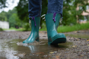 Woman wearing turquoise rubber boots walking in puddle outdoors, closeup