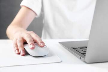 Fototapeta premium Woman using computer mouse while working with laptop at white table, closeup
