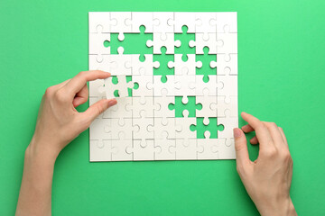Woman solving white puzzle on green background, closeup