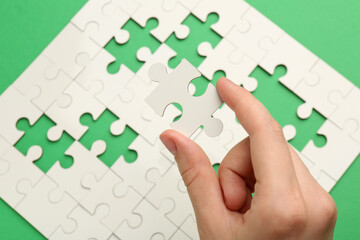 Woman solving white puzzle on green background, closeup