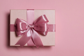 Gift box with bow on dusty pink background, top view