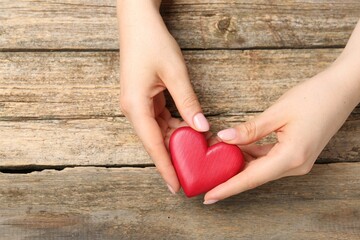 Woman with red decorative heart at wooden table, top view. Space for text