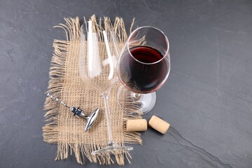Corkscrew with metal handle, corks and glass of wine on grey table