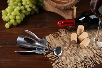Wing corkscrew, corks, bottle of wine, glass and grapes on wooden table