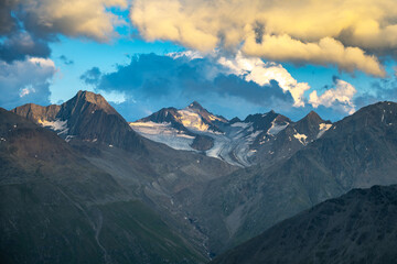 Fototapeta premium The stunning peaks of the Alps rise dramatically against a vibrant sky during evening twilight. The sunlight casts soft shadows on rocky landscapes, highlighting the beauty of nature's untouched