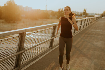 Determined runner jogs along a sunlit bridge during the golden hour, blending fitness and serenity in an urban landscape