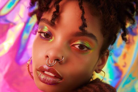 Portrait of model with a septum piercing, highlighting the unique jewelry and the expression on their face, set against a vibrant, colorful backdrop.