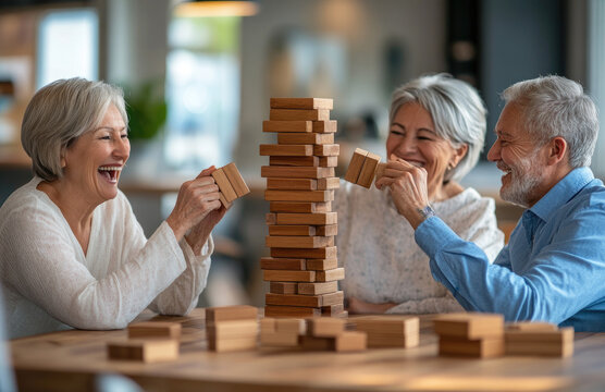 A group of happy elderly friends playing Jenga at the table in coffee shop, having fun and laughing together