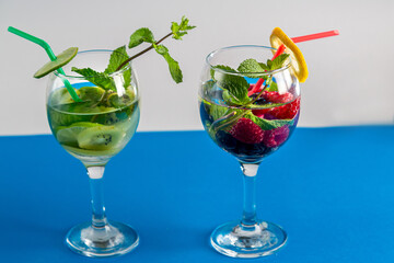 Two Glasses with cocktail kiwi raspberry mint lime with ice on blue background