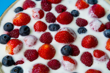In a plate with freshly whipped cream juicy berries strawberries raspberries and blueberries close-up