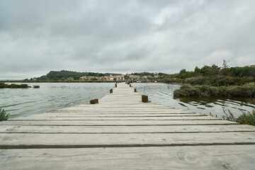 Wooden walkway crossing a lake surrounded by water and on the horizon the land with the sky covered with clouds with a storm