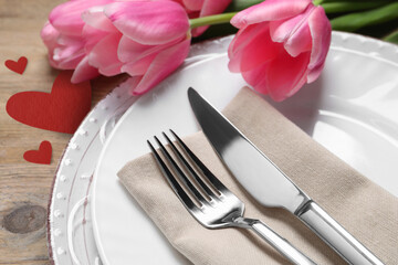 Table setting for romantic Valentine's day celebration. Plates, cutlery, flowers and hearts on wooden table, closeup