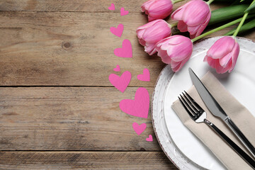 Table setting for romantic Valentine's day celebration, top view. Plates, cutlery, flowers and hearts on wooden table, space for text