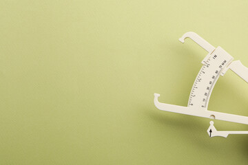 Plastic body fat caliper on light green background. Space for text