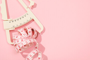 Body fat caliper and measuring tape on pink background, top view. Space for text
