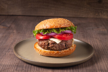Homemade delicious hamburger with beef, onion, tomato, lettuce and cheese. Fresh burger close up on wooden rustic table with potato fries. Cheeseburger. Burger.