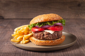 Homemade delicious hamburger with beef, onion, tomato, lettuce and cheese. Fresh burger close up on wooden rustic table with potato fries. Cheeseburger. Burger.