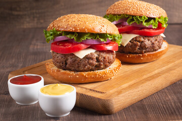 Homemade delicious hamburger with beef, onion, tomato, lettuce and cheese. Fresh burger close up on wooden rustic table with potato fries. Cheeseburger. Burger.