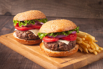 Homemade delicious hamburger with beef, onion, tomato, lettuce and cheese. Fresh burger close up on wooden rustic table with potato fries. Cheeseburger. Burger.