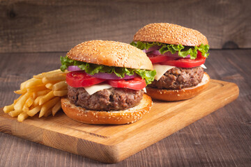 Homemade delicious hamburger with beef, onion, tomato, lettuce and cheese. Fresh burger close up on wooden rustic table with potato fries. Cheeseburger. Burger.