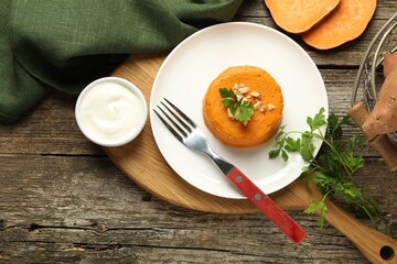 Tasty mashed sweet potato, parsley and walnuts served with sauce on wooden table, flat lay