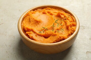 Tasty mashed sweet potato and thyme in bowl on grey textured table, closeup