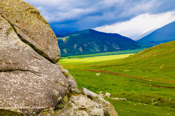large rock in front of picturesque green mountains background with storm clouds above