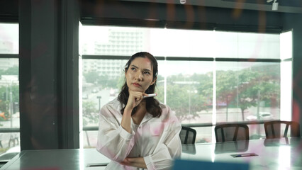 Beautiful female leader thinking about start up project in front of glass board. Smiling young...