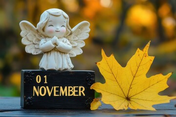 A cute angel figurine sits by an autumn leaf and a calendar which marks November 1.